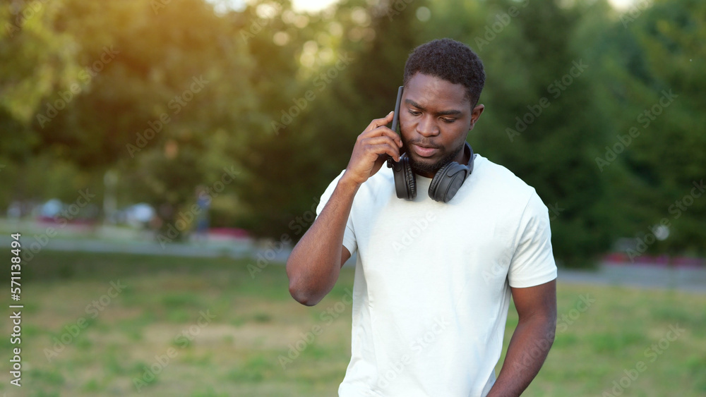 Black man talks on smartphone with friend discussing holiday. African American tourist enjoys walking in green park talking with mate, sunlight Black man talks on smartphone with friend discussing holiday. African American tourist enjoys walking in green park talking with mate, sunlight