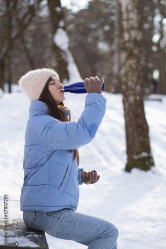 Portrait of young woman in warm clothes in winter forest. Drinking hot tea