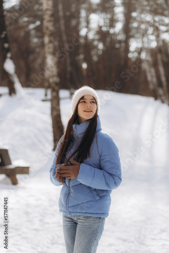 A beautiful young woman in a blue jacket is walking in a winter park.