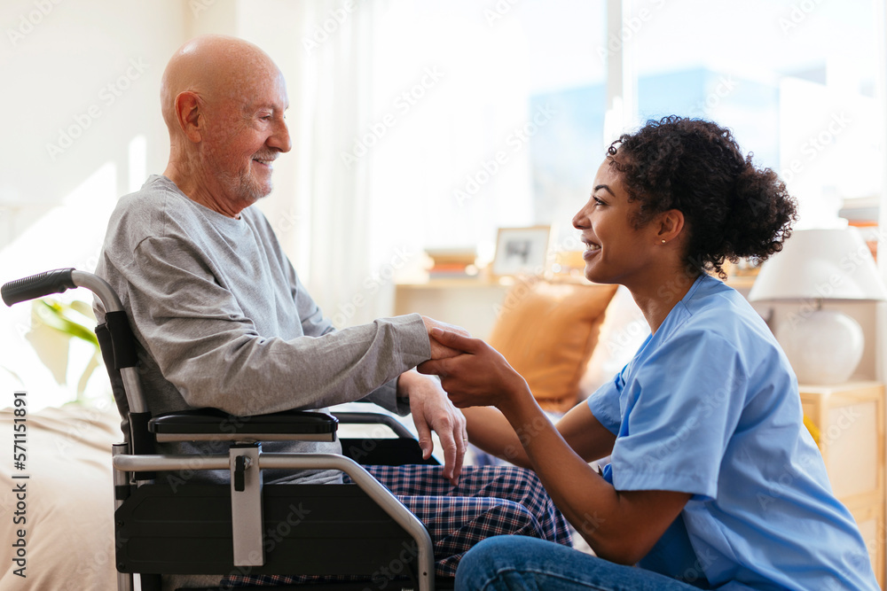 Happy physical therapist holding hand of senior man sitting on wheelchair Happy physical therapist holding hand of senior man sitting on wheelchair