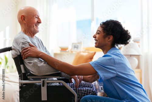 Happy physiotherapist talking to senior man sitting on wheelchair photo
