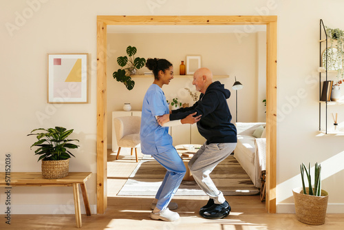 Home caregiver assisting senior man in exercising at home
