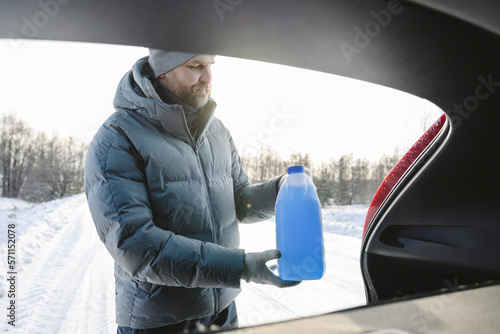 Man taking bottle of car anti-freeze liquid from trunk in winter photo