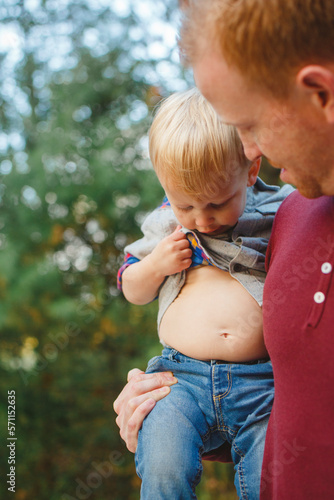 A little boy in dad's arms lifts his shirt to check out his stomach