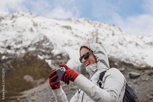 Woman hiker with uses cell phone camera on windy day in mountains. photo