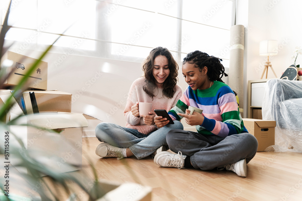 Happy young woman sharing mobile phone with friend at home Happy young woman sharing mobile phone with friend at home