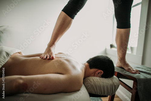 massage therapist uses ashiatsu method feet to treat patient's back