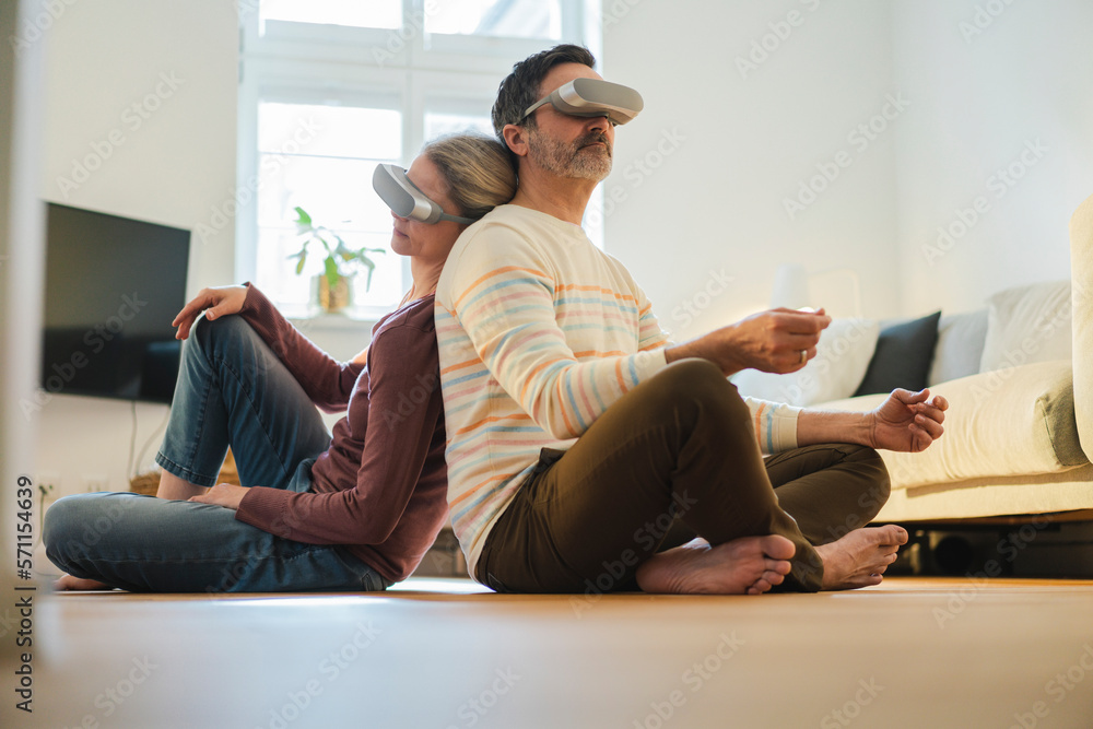 Man and woman wearing virtual reality headset sitting back to back at home Man and woman wearing virtual reality headset sitting back to back at home