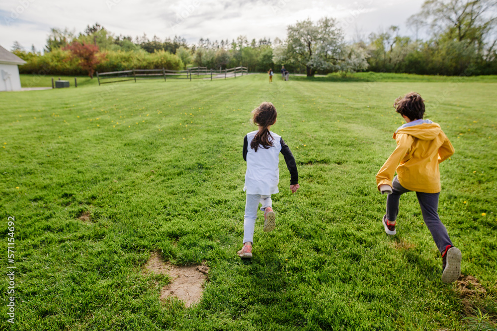 Three children run through a field at springtime, one far ahead Three children run through a field at springtime, one far ahead