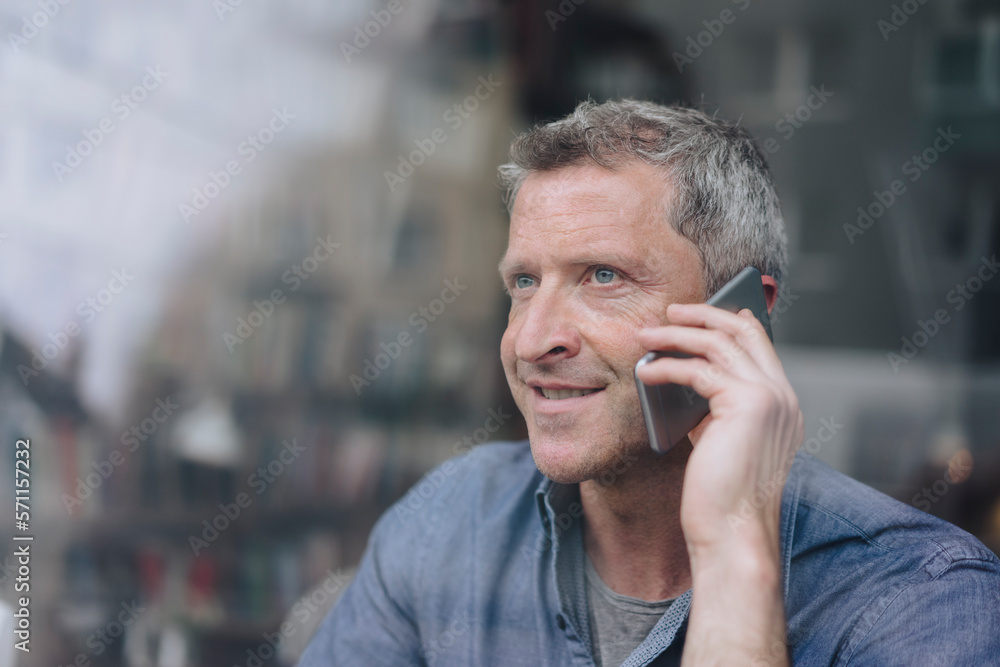 Smiling man talking on mobile phone seen through glass Smiling man talking on mobile phone seen through glass
