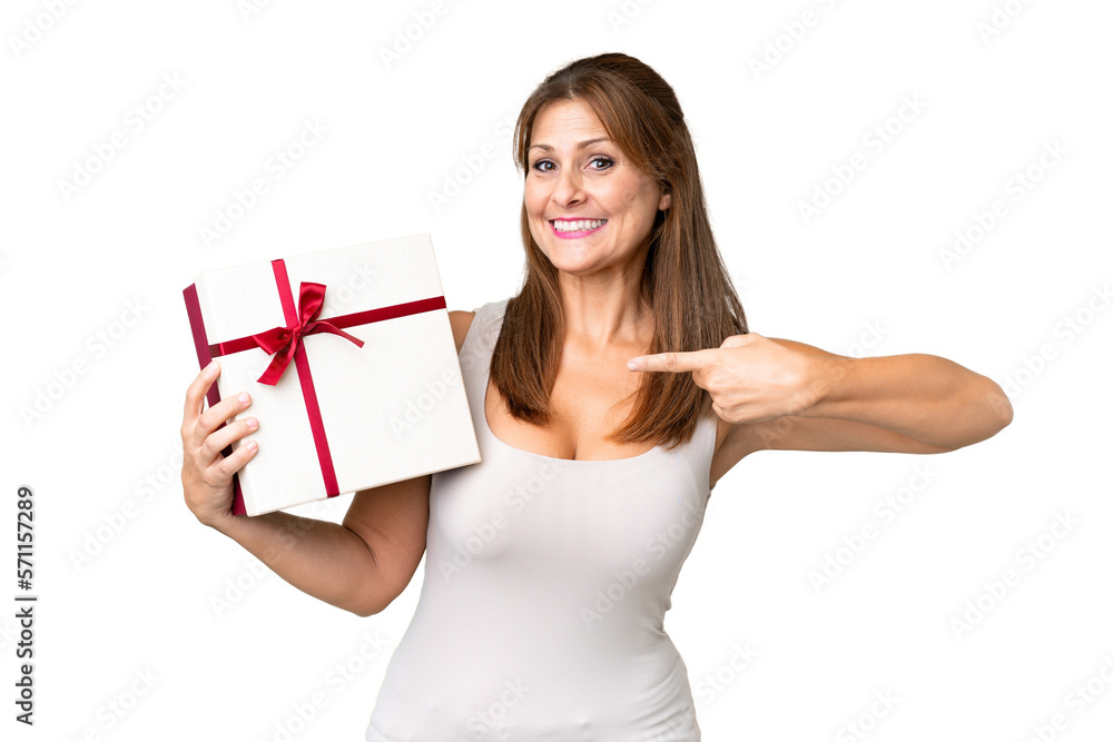 Middle age caucasian woman holding a gift over isolated background and pointing it Middle age caucasian woman holding a gift over isolated background and pointing it