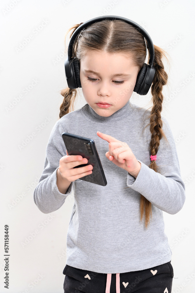 A girl with headphones and a phone on a white background, a girl with pigtails listens to music in headphones, photo with copy space. A girl with headphones and a phone on a white background, a girl with pigtails listens to music in headphones, photo with copy space.