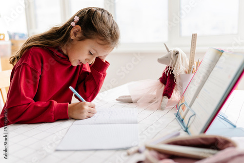 Girl doing homework sitting at table photo