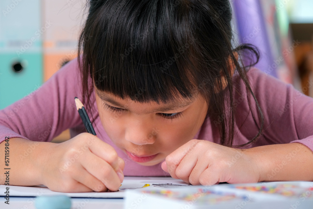 Happy little girl drawing with colored pencils on paper sitting at table in her room at home. Creativity and development of fine motor skills. Happy little girl drawing with colored pencils on paper sitting at table in her room at home. Creativity and development of fine motor skills.