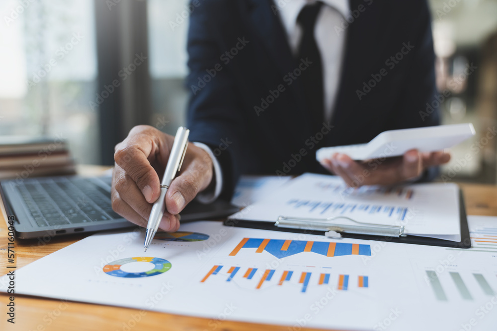 Asian businessman working in the office, calculating financial reports, organizing paperwork using a laptop and calculator as an aid.management concept accounting. Asian businessman working in the office, calculating financial reports, organizing paperwork using a laptop and calculator as an aid.management concept accounting.