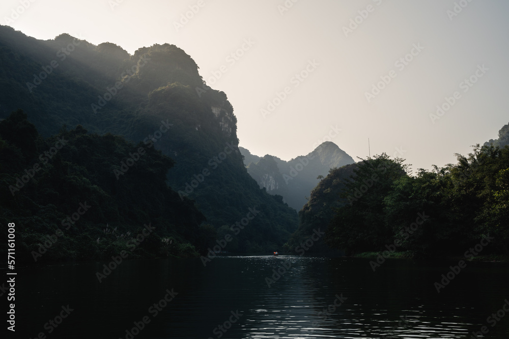 On a row boat tour in the beautiful valley of Trang An (Ninh Binh) Vietnam. Sun rays breaking through lime stone rocks with deep tropical forest during sunset.