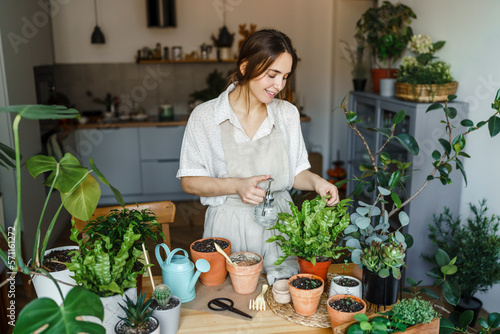 Smiling woman spraying water on plant at home