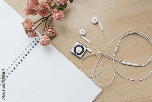 Top view of a wooden table on which lies an open notebook for notes on the rings dry roses and a small old player with headphones, vintage style copy space, mockup.