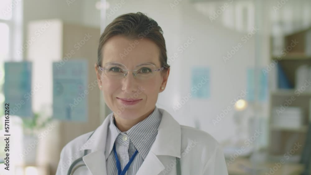 Portrait of female doctor in white coat and eyeglasses smiling and posing for camera at work in clinic Portrait of female doctor in white coat and eyeglasses smiling and posing for camera at work in clinic