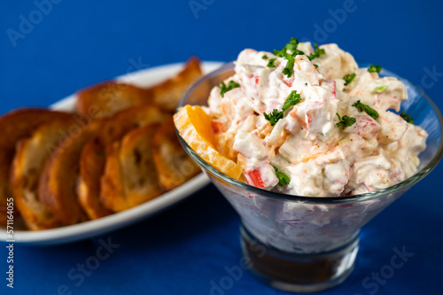 Crab salad in glass bowl, fried toast on plate on blue background.