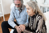 Hand touching sad older caucasian couple at home 