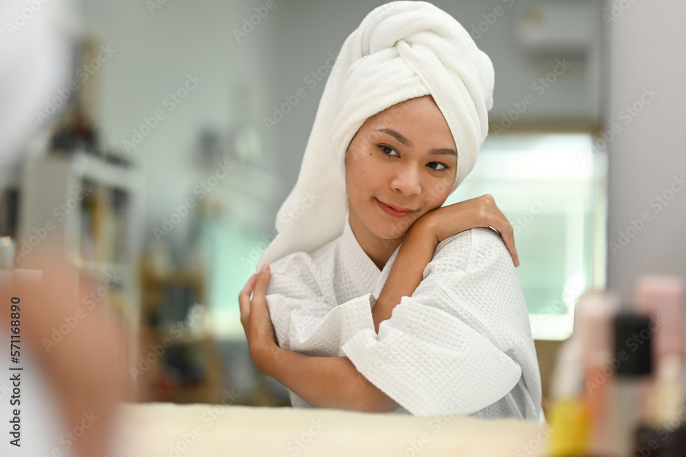Beautiful young woman with towel on head hugging herself and looking in mirror. Self care and self esteem concept Beautiful young woman with towel on head hugging herself and looking in mirror. Self care and self esteem concept