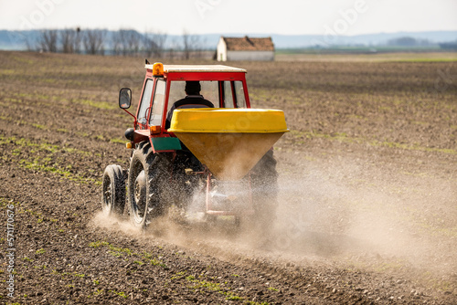 Farmer in an agricultural tractor at a farm applying fertilizers to an arable field, a necessary task