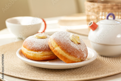 Breakfast table with Krapfen or berliner, or doughnut, or bombolone with cream filling. Tea cup and tea pot.