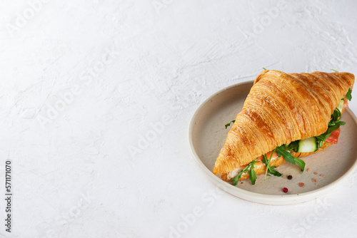 Croissant sandwich with salmon, cream cheese and arugula in a plate. Copy space.