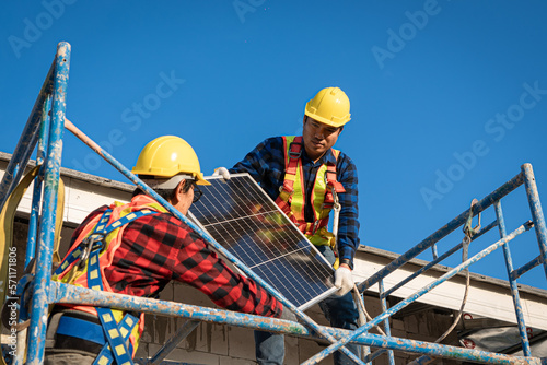 Engineers in helmets installing solar panel system outdoors. technician use a the Electric drill installing the solar panels at roof top of home and home office. 