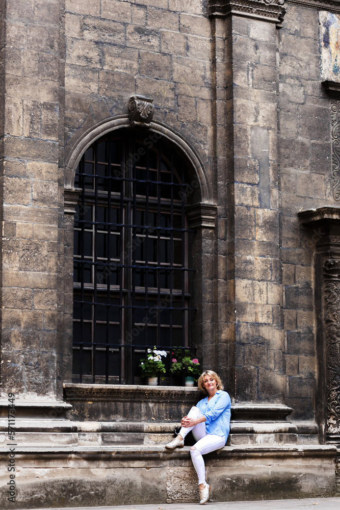 young blond woman sits against the background of a Gothic facade