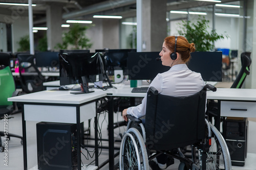 Red-haired caucasian woman in a wheelchair talking on a headset. Female call center worker at her desk.