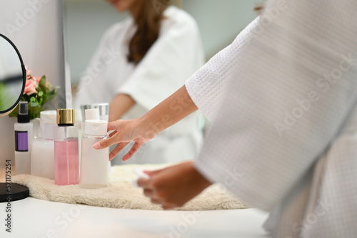 Cropped shot of woman in bathrobe choosing cosmetic package on dresser table. Beauty treatment and self care concept