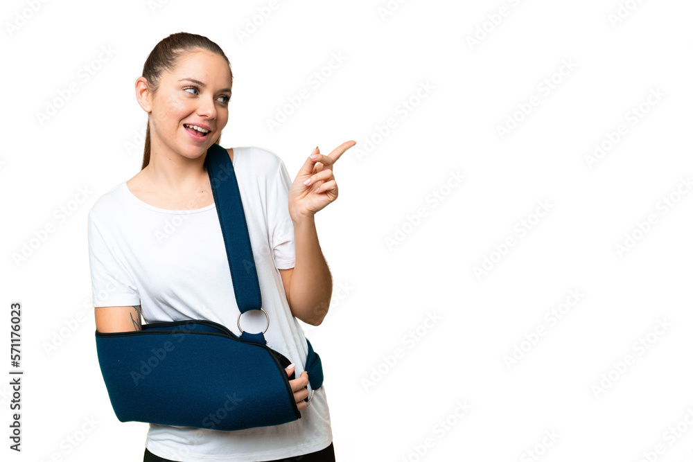 Young blonde woman with broken arm and wearing a sling over isolated chroma key background pointing finger to the side and presenting a product Young blonde woman with broken arm and wearing a sling over isolated chroma key background pointing finger to the side and presenting a product