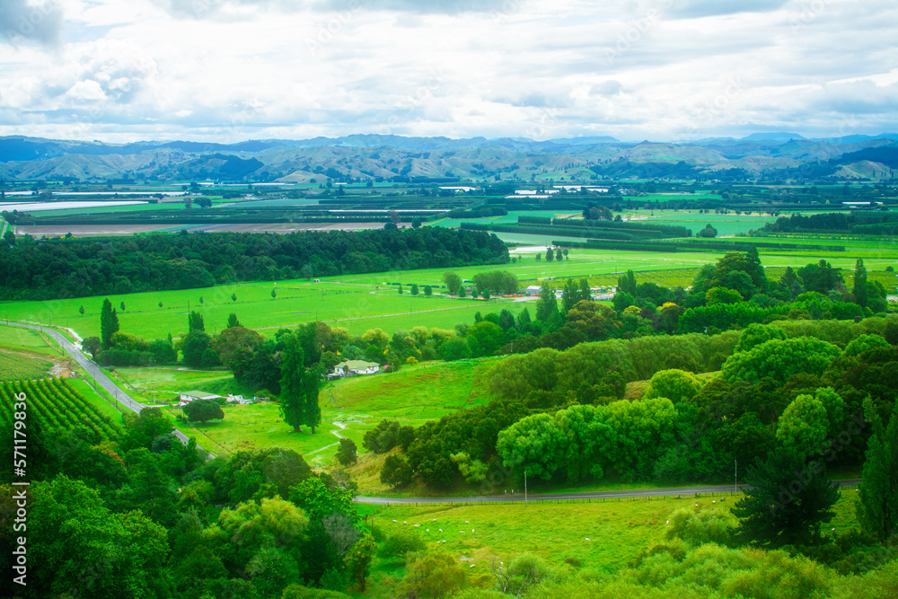 Aerial view over lush green farmland and distand mountain range under cloudy sky. Breathtaking New Zealand Landscape. Greys Hill Lookout, Gisborne, North Island, New Zealand