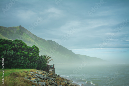 Thick mist over ocean beach surrounded by mighty rugged mountains. Cloudy day at Makorori beach, Gisborne, North Island, New Zealand photo