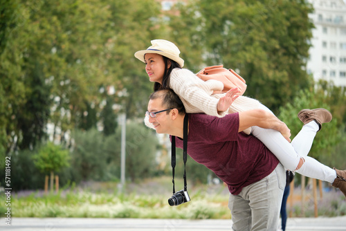 Multiracial couple of tourists piggyback with spread arms like plane wings. Sightseeing in Madrid, Spain.
