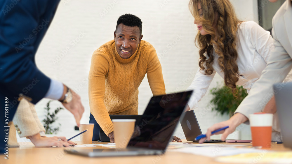 Obraz premium Black male team leader at business meeting in an office, discussing business affairs with other workers, papers with charts and gadgets on the table
