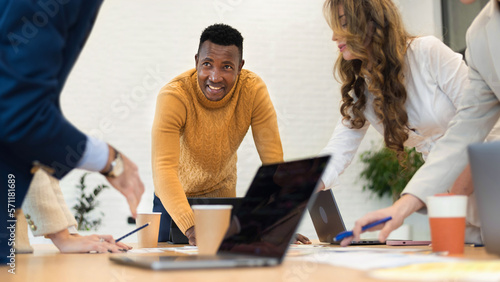 Black male team leader at business meeting in an office, discussing business affairs with other workers, papers with charts and gadgets on the table