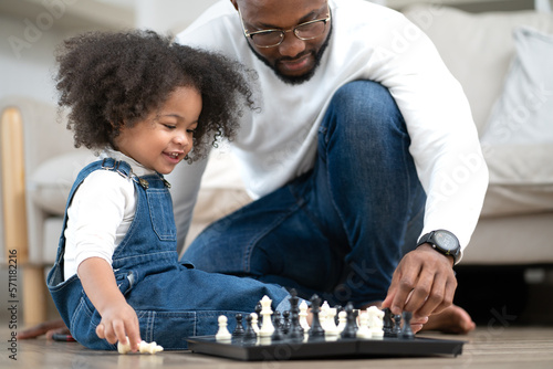 Cute little girl playing chess board as her father sitting by. Multiracial family happy leisure together with a young daughter kid at home. Multiethnic child has fun playing chess pieces with her dad.
