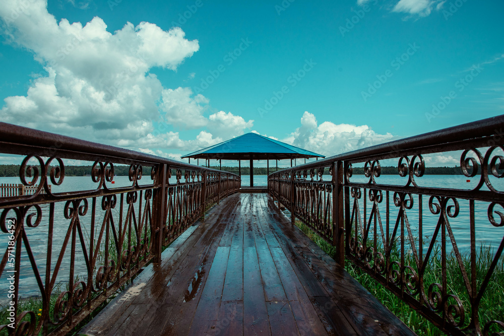 A blue gazebo on the shore of the lake, a small wooden pier, a blue lake.
