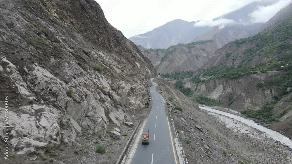 Rickshaw Vehicle on Road in Mountains of Northern Pakistan. Cinematic Aerial View of Hunza Valley Landscape and River Canyon Rickshaw Vehicle on Road in Mountains of Northern Pakistan. Cinematic Aerial View of Hunza Valley Landscape and River Canyon