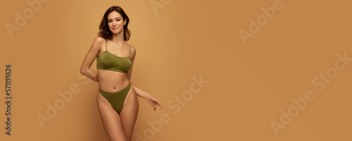 Adorable beautiful caucasian woman with slim fit figure in olive color inner wear posing on yellow studio background. Concept of female body, health, sport, spa, ad