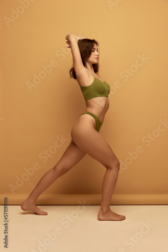 Portrait of young slim beautiful girl wearing green color underwear posing over brown background. Concept of beauty, body and skin care, healthy eating