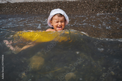 Fototapeta Naklejka Na Ścianę i Meble -  Baby boy swims in a yellow inflatable circle in the sea. The child is happy and laughing.