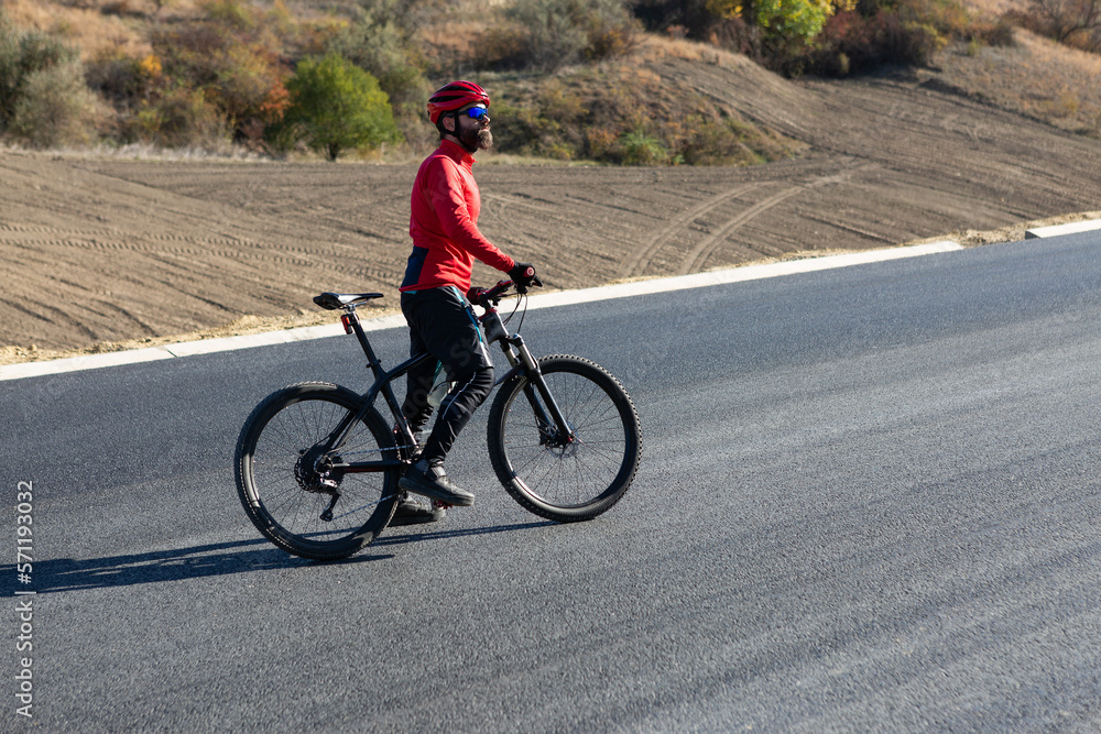 Obraz premium Cyclist riding bicycle on road against clear sky. A man in an outfit stands with a bicycle on an autumn sunny day.