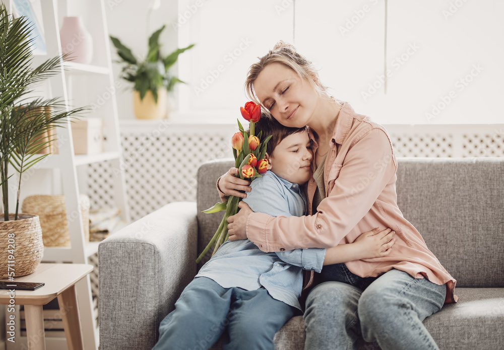 © candy1812 - Cute boy sitting on the sofa with mom and giving a bouquet of tulips to her.