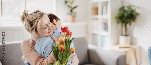 Fotografia Cute boy sitting on the sofa with mom and giving a bouquet of tulips to her