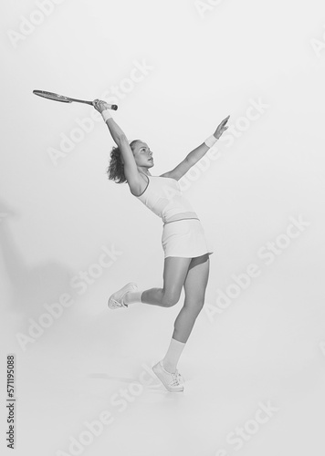 Black and white portrait of young sportive woman in white uniform playing badminton. Retro vintage sport, fashion, art