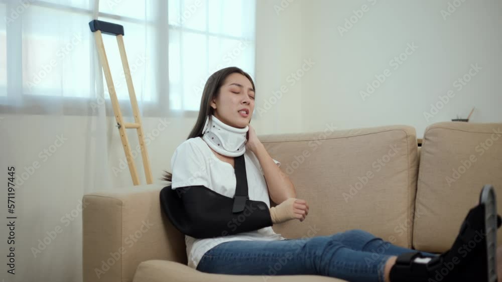 Woman suffered pain from accident fracture broken bone injury with leg splints in cast, neck splints collar, arm splints, sling support arm in living room. Social security and health insurance. Woman suffered pain from accident fracture broken bone injury with leg splints in cast, neck splints collar, arm splints, sling support arm in living room. Social security and health insurance.